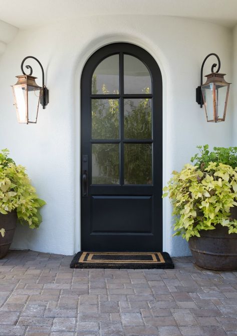 Black arched front door flanked by Old World lanterns and white Stucco house exterior. Jaimee Rose Interiors. Black Arch Front Door, Arch Front Door Exterior Modern, Arched Exterior Doors Entrance, Black Arch Door, Black Arched Front Door, Arch Transom Front Door, Arched Doorway Exterior, Arch Front Door Exterior, White Door