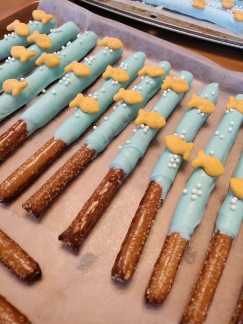 White chocolate dipped pretzel rods with white sprinkles and goldfish crackers on them. The white chocolate is dyed aqua blue. Fishing First Birthday Party Favors, Fishing Birthday Party Food Ideas, The Big One Wave First Birthday Food, Fish Theme Party Food, The Big One Food Ideas, Ofishally Five Birthday, 1st Birthday Boy Fishing Theme, Oh Fishally One Birthday Decorations Diy, The Big One Party Favors