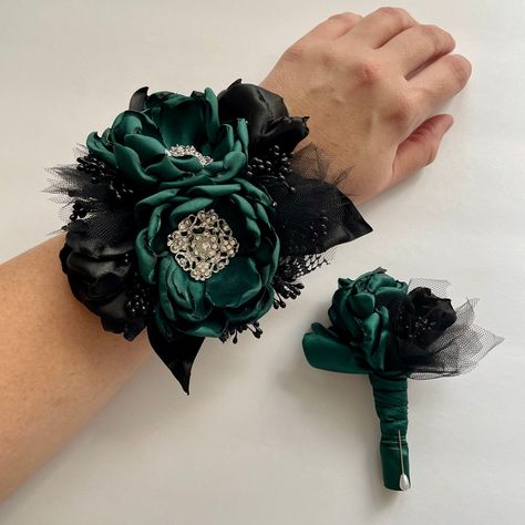 Corsage: large cluster of black and jewel green flowers. Side flowers and tulle details. Black stamen. Lace and black satin leaves. On a black elastic wrist band.  Boutonniere: main flower in jewel green. Small side flower in black satin and tulle details. Wrapped in layers of jewel green satin. Comes with a pearl head corsage pin. Message me with any questions! Emerald Green And Black Corsage, Black And Green Corsage, Emerald Green Corsage And Boutonniere, Corsage Prom Green, Dark Green Corsage, Green Corsage And Boutonniere, Green Prom Corsage, Emerald Green Corsage, Black Corsage And Boutonniere