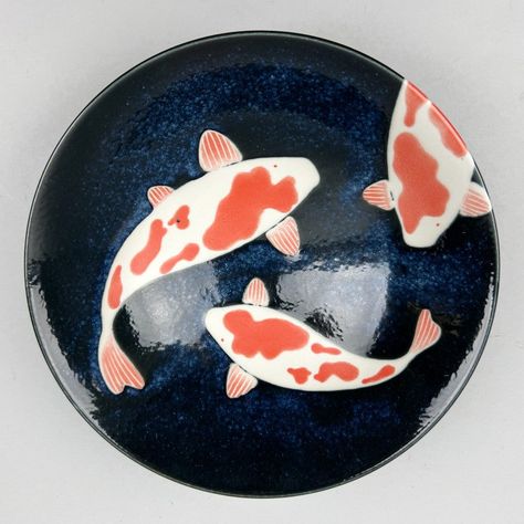 Enhance your tablescape with an authentic Japanese touch using the Koi Gunjo Ramen Shallow Flared Bowl Serving Bowl. Featuring a deep navy glaze and iconic images of three beautiful swimming koi fish, perfect for serving ramen, entrees, or as a decorative piece. Directly sourcing from Japan. SPECS: Material: Ceramics Size: 9.75"dia. x 3" height (48 oz) Weight: 1.58 pounds Dishwasher and microwave safe New Made in Japan Item Code: J6201 SPECS: Material: Ceramics Size: 9 3/4" dia. x 3" tall (48 oz Japan Ceramic Pottery, Koi Fish Ceramic Art, Designs For Ceramics, Japanese Ramen Bowl Ceramic, Plate Inspiration, Koi Pottery Painting, Ceramics Japanese, Clay Dish Painting Ideas, Slab Plates Ceramics