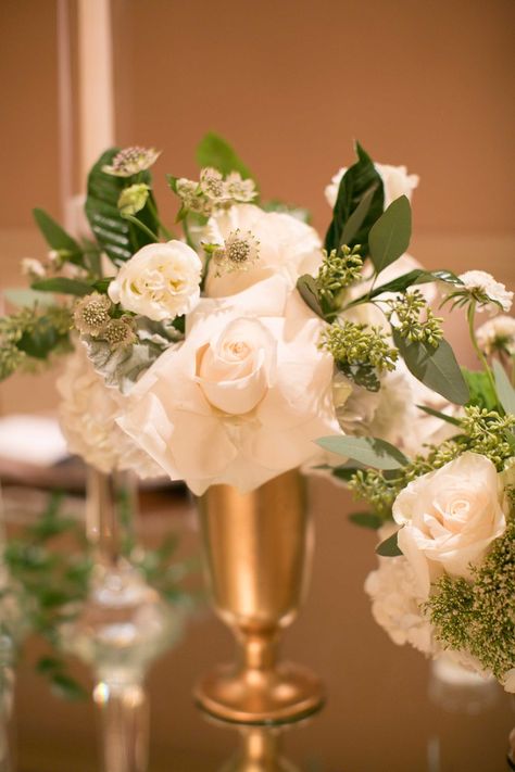 Mini Green & Ivory Floral Arrangement in Gold Vase | Photo: Marianne Lozano Photography. White And Gold Table Centerpieces With Glass Cylenderys, Gold Vase White Flower Centerpieces, White Florals In Gold Compote Vase Wedding Centerpiece, Gold Terrarium Centerpiece, Orchid In Gold Vase, Event Centerpieces, Simple Beach Wedding, Gold Vase, Wedding Greenery