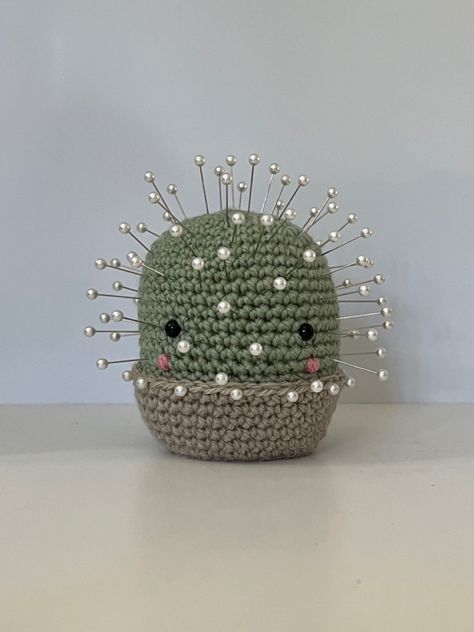 pale green crochet amigurumi cactus with plastic eyes and pink blush in a beige crocheted pot. the cactus is a pin cushion and has many pearl head pins halfway stuck in it. the background is cream/white. Crochet Cactus Pin Cushion, Cactus Pin Cushion, Crochet Cactus, Pearl Pin, Pin Cushion, Head Pins, Pin Cushions, Handmade Crochet, Crochet Amigurumi