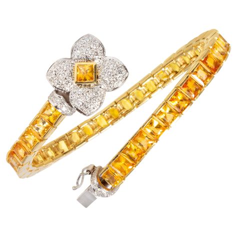 The color line bracelet features a row of especially calibrated baguette princess-cut yellow sapphires (approximately 19 carats) flanked by a bridge set with round diamonds. The clasp consists of a flower design set with round diamonds. The total weight of round diamonds is approximately 1 carat (F/G-VVS). The design is accented by the use of both white and yellow 18 carat gold. The bracelet was handmade in Italy in our own workshop according to an original design by Ella Gafter. It can be stack Diamond Bracelet Design, Bracelet Tennis, White Gold Sapphire, Fancy Diamonds, Sapphire Bracelet, Elegant Bracelet, Yellow Gold Bracelet, A Bridge, Lovely Jewellery