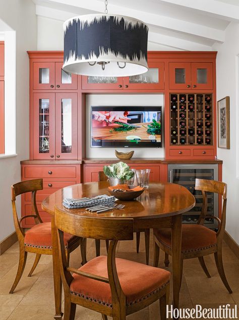 The custom light fixture is almost as large as the breakfast table. "With the high ceiling, I had enough space, and the Clarence House fabric I used for the shade — Operato — needed that scale," says designer Melanie Coddington. Antique chairs covered in Holly Hunt's High Cotton surround an antique table. Sub-Zero wine refrigerator. Samsung television. Roswell knobs by Rocky Mountain Hardware on cabinets. Floor is Alterra stone from Marble Systems.   - HouseBeautiful.com Orange Kitchen Ideas, Burnt Orange Kitchen, Cupcake Kitchen Decor, Dining Room Teal, Orange Dining Room, Kitchen Ideas Decor, Orange Kitchen Decor, Orange Furniture, Furnitur Ruang Keluarga