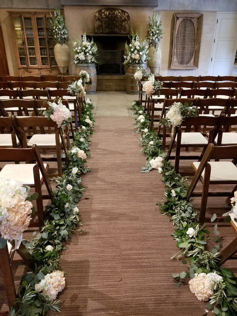 Sonoma Wedding Ramekins - Indoor wedding aisle floral featuring eucalyptus garland lining the aisle dotted with ivory and blush flowers. Chair bouquets, Altar flowers on wine barrels. #Ramekinswedding #Sonomawedding #aislefloral #winebarreltoppers Wedding Aisle Garland Decor, Aile Flowers Wedding, Wedding Aisle Indoor Decorations, Eucalyptus Aisle Runner, Eucalyptus Lined Aisle, Wedding Aisle Eucalyptus, Wedding Aisle Garland, Wedding Aisle Florals Indoor, Elegant Aisle Decorations Wedding