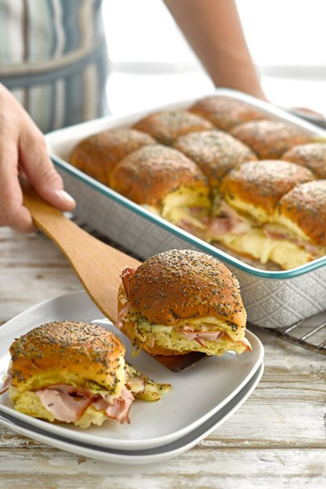 A person placing a ham and cheese slider roll on a plate with a wooden spatula on a table. Brioche Slider Buns Recipe, Ham And Cheese Brioche Sliders, Fancy Ham Sandwiches, Brioche Rolls Sandwiches, Brioche Bun Sandwich Ideas, Brioche Sandwich Ideas, Brioche Buns Sandwiches, Brioche Sliders, Brioche Sandwich