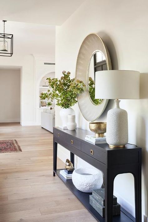 An Aerin Culloden Lamp illuminates a black console table under a large round gray shagreen mirror. Black Console Table, Console Table Design, Console Table Decorating, Entryway Table Decor, Foyer Design, Home Entrance Decor, House Entrance, Decor Rustic, Entryway Decor