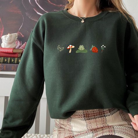 These unisex frog sweatshirts are made for comfort. Made of an 8 oz cotton/poly blend, these are perfect for cooler weather. Look cute and stay cozy in this cottagecore sweater! There are no itchy side seams on these sweaters, making them pleasant to wear. -Unisex Sweatshirt Size Options- Please make sure to scroll through the photos to see the size chart. These are a unisex fit so they will be looser if you order your normal women's size. - When Can I Expect My Order - Processing Time: 1-3 days Green Sweaters, Casual Cottagecore Outfits Winter, Sweaters Cottagecore, Clothes Fall, Frog Clothes, Cottagecore Outfit Winter, Masc Cottagecore, Cottagecore Hoodie, Goth Cottagecore Aesthetic