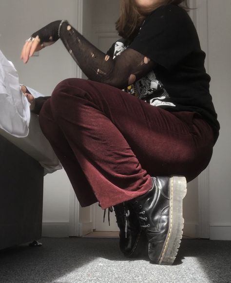 A mid-size person/girl wearing a black shirt with a white print-on, a black ripped tights top under it, dark red velvet pants, black platform dr. Martens and multiple crystal rings and bracelets. 	The person is also wearing multiple silver necklaces; one in form of a skull, a big cross, and one in form of a moon, a long black bead necklace and a black lace choker. Two Toned Pants Outfits, Red Velvet Jeans Outfit, Doc Martens Outfit Goth, Academic Goth Aesthetic, Doc Martens Outfit Alt, Vampire Aesthetic Outfit Casual, Red Pants Aesthetic, How To Style Velvet Pants, Casual Vampire Goth Outfits