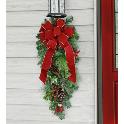 This beautiful pine door swag can be used on a door, an outside light fixture, mantel decoration, stair railings or windows to enhance your holiday season. Get more than one! Created with artificial pine, pine cones, berries and a handmade red velvet bow with gold edge. The Holiday Aisle® | The Holiday Aisle® Faux Pine Teardrop Swag 36.0 H x 5.0 W x 10.0 D in green / red | 30" H X 9" D X 10" L | Wayfair Christmas Swag Outdoor Light, Porch Light Christmas Swag, Red And Green Outdoor Christmas Decor, Lantern Swags Christmas, Swag Door Wreath, Christmas Swags For Outdoor Lights, Christmas Swag For Outdoor Lights, Front Door Decor For Christmas, Indoor Christmas Door Decorations