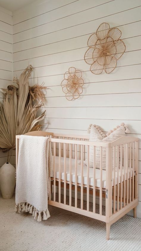 A cozy nursery with a light wood crib, textured white quilt, and decorative rattan flower wall art. The design includes neutral tones, shiplap walls, and dried palm leaves for a natural, minimalist aesthetic. Minimalist Nursery Ideas, Baby Girl Nursery Ideas, Girl Nursery Ideas, Nursery Inspiration Girl, Textured Pillows, Rattan Wall, Minimalist Nursery, Girls Nursery, Baby Girl Nursery