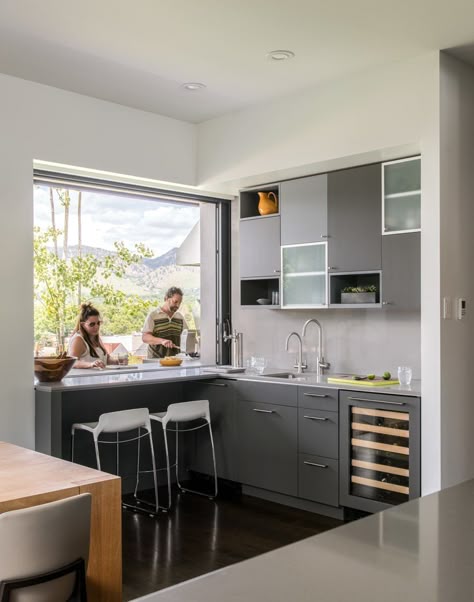 A pocket window in the kitchen allows for a double-sided bar area, with access to the outside grill. "It’s a great place to sit and drink your morning coffee and enjoy the views," said Goff, who placed two Tiffany counter stools at the pass-through bar. The kitchen cabinets are a mixture of rift-cut white oak and cabinets painted in Benjamin Moore’s low-gloss Iron Mountain hue, with Caesarstone countertops. Kitchen Pass Through Window, Kitchen Window Bar, Kitchen Pass Through, Kitchen Pass, Pass Through Window, Kitchen Window Design, Target Kitchen, Window Bars, Indoor Outdoor Kitchen