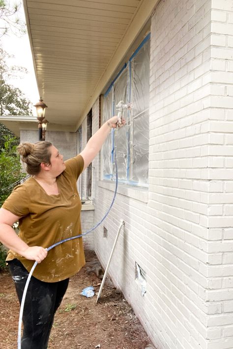 Woman using Graco Magnum 262800 X5 Stand Airless Paint Sprayer to paint exterior brick home white with paint sprayer. Instructions of how to paint a brick house with pros and cons. Blue painters tape with sheeting covering windows. Painted White Brick House, Painting Brick Exterior, Red Brick Paint, White Brick Exterior, Brick Exterior Makeover, Brick Painted White, House With Front Porch, House Exterior Before And After, Painted Brick House Exterior