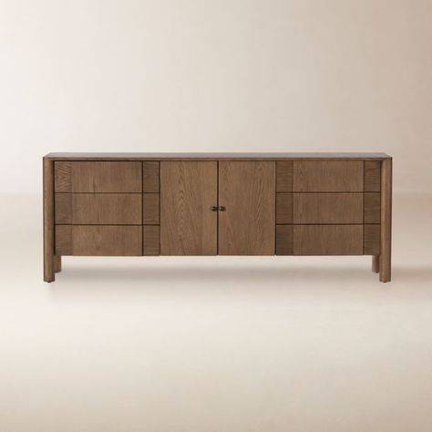 Stately oak credenza sports clean lines and abundant storage. Warm, tan-toned oak frame opens to reveal a center shelf flanked by three spacious drawers on either side. Bronze gunmetal-finish hardware and carved oak drawer pulls imbue the piece with the spirit of a vintage find.  -Solid oak and oak veneer -Six drawers and center interior shelving -Rear cutout for cord management -Made in USA of Imported Materials Pollard 78" Tan Oak Credenza Cb2 Credenza, Teak Credenza Living Room, 80” Tv Credenza, Oak Credenza, 70” Media Console, 105” Media Console, Media Credenza, Walnut Credenza, Wood Media Console