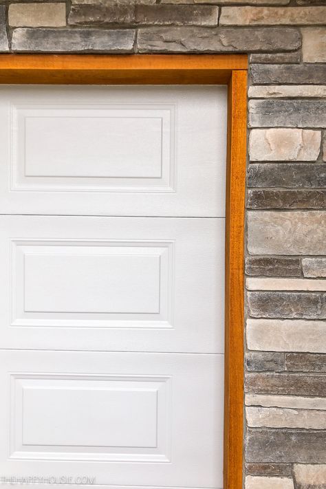 A white garage door, cedar trim and stone work. Cedar Trim Around Garage Door, Wood Trim Around Garage Door, Wood Trim Garage Door, White Garage Doors With Black Trim, Garage Trim Ideas Exterior, White House Cedar Accents, Cedar Trim Exterior, Garage Door Trim Ideas, Front Yard Exterior