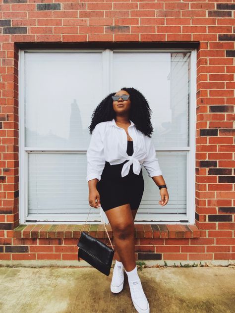 Black woman wearing black bike shorts, black tank under a white button down shirt that has been tied at the waist. She is accessorized with black sunglasses and a black purse with a gold chain strap. Short Black Dress With Sneakers, Bike Shorts Outfit Summer Plus Size, How To Style Biker Shorts, White Platform Converse Outfit, Converse Platform Outfit, Style A White Shirt, Platform Converse Outfit, Shirt Under Dress, Platform Outfit