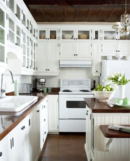 Stunning white kitchen design with off-white beadboard kitchen cabinets, glass-front cabinets, white subway tiles backsplash, butcher block countertops, white appliances and kitchen island. by Susan Butcher Block Countertops White Appliances, White Kitchen Cabinets With Butcher Block, Nice Kitchens, Kitchen Restoration, Block Countertops, White Kitchen Appliances, Butcher Block Kitchen, White Tile Backsplash, Cabinet Paint