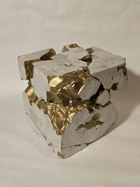 a Rectangular prism sculpture composed of concrete, with sections deliberately fragmented. The crevices and fractures within the cube are filled with a gold pigment, giving the impression that the cube has gold veins running through it. The contrast between the rough, industrial gray of the concrete and the luxurious shiny gold Reference the Japanese art of kintsugi, where broken pottery is repaired with gold or a gold-like substance, emphasizing the beauty in imperfection.  6"x6"x5.5" weighs ~9 Cubic Sculpture, Gold Reference, Beauty In Imperfection, Gold Veins, Rectangular Prism, Retail Design, Art Object, Japanese Art, Sculpture Art