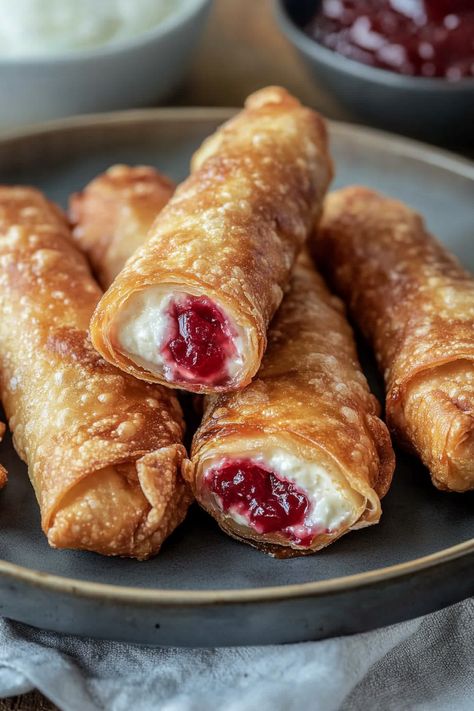 Cherry Cheesecake Egg Rolls offer a delightful twist on the traditional Asian appetizer! Packed with a tart cherry filling and luscious cream cheese, these crispy treats are easy to prepare and can be pan-fried, air-fried, or baked. Wrapped in wonton skins and sprinkled with cinnamon sugar, these dessert egg rolls are a quick and delightful Cheesecake Wontons Air Fryer, Apple Cream Cheese Egg Rolls, Crispy Cherry Cheesecake Egg Rolls, Cherry Egg Rolls, Cherry Cheesecake Rolls, Cherry Cheesecake Egg Roll Recipe, Cherry Cream Cheese Egg Rolls, Wonton Deserts, Sweet Egg Rolls Desserts