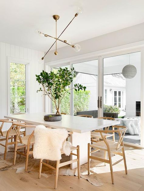 Dining room features a white wooden dining table with tan wishbone chairs upton a light brown cowhide rug, lit by a brass chandelier. Wishbone Chair Dining Room, Wishbone Chair Dining, Tamara Magel, Hampton Home, Cottage Dining Rooms, Transitional Dining, Reclaimed Wood Table, Inspired Interiors, White Dining Table