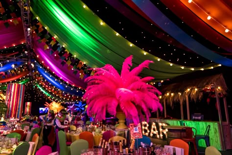 To create a Rio Carnival theme we dressed the ceiling with hundreds of metres of bunting, ribbon and flags, while on the ground, Brazilian dance troops with feathered headdresses and sequinned costumes paraded between a sea of brightly coloured tables which were dressed with a number of Carnival themed table centres. From illuminated LED palm trees and arrangements of bird of paradise and palms, to coloured candelabra and rotating ribbon chandeliers, guests were fully emerged in the theme. Carnivale Prom Theme, Rio Carnival Theme Party Outfit, Brazil Party Decorations, Brazilian Party Decorations, Rio Homecoming Theme, Rio Prom Theme, Rio Carnival Theme Party Decorations, Carnaval Theme Party, Carnival Brazil Party