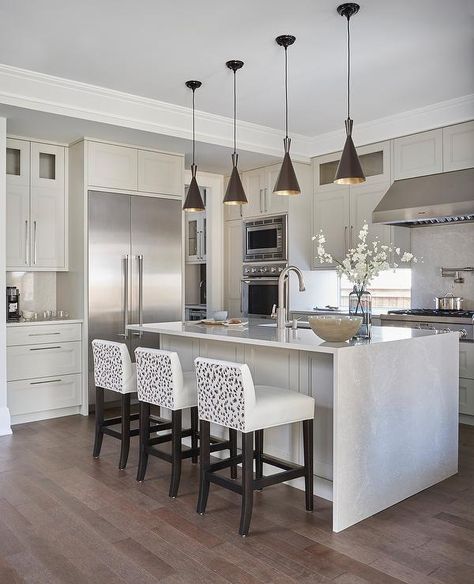 Tom Dixon Beat Lights elegantly hang over a light gray stone island with a one-sided waterfall feature. Transitional Kitchen Lighting, Countertop Quartz, Waterfall Island Kitchen, Tom Dixon Beat, Waterfall Countertop, Unique Kitchen Design, Waterfall Island, Grey Kitchen Island, Lighting Fixtures Kitchen Island