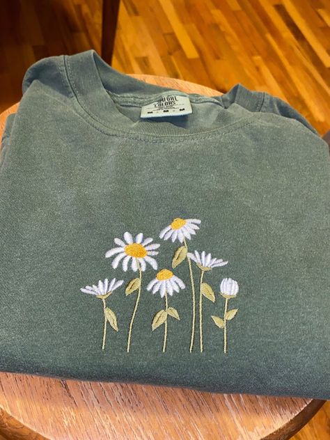 Vibrant daisies embroidered on a moss green T-shirt !! :)   The T-shirts I use are comfort colors brand in adult unisex sizing! Hand Embroidery T Shirt Ideas, Green Shirt Embroidery, Embroidery On T Shirt, Embroidered Clothes Ideas, Embroider Daisies, Embroidery Shirt Ideas, Embroidery Ideas Clothes, Embroidering Clothes, Embroidery Tshirts