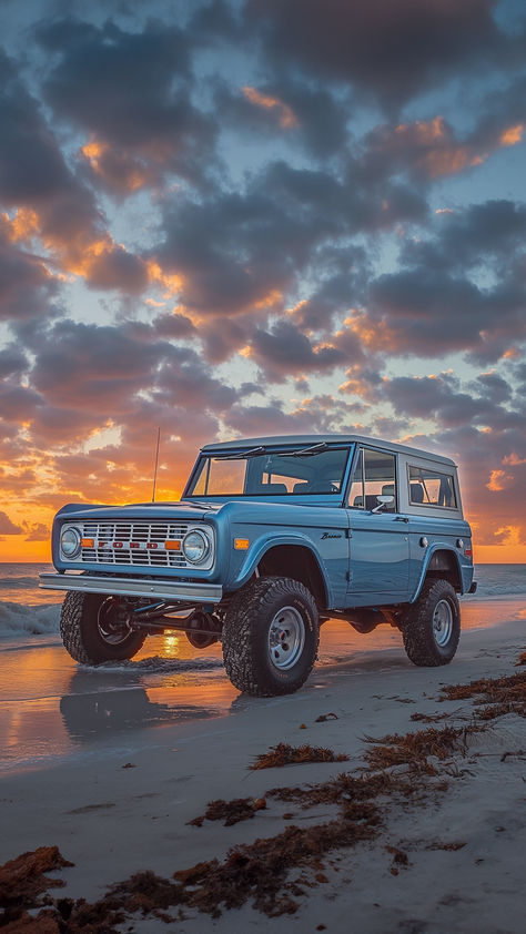 A classic blue Ford Bronco stands poised on the shoreline, with waves gently lapping at its tires, against a breathtaking backdrop of a sunset sky ablaze with warm orange and cool blue hues. Blue Bronco, Blue Ford Bronco Aesthetic, Beach Bronco, Vintage Bronco, Vintage Bronco Aesthetic, Ford Bronco Aesthetic, Vintage Ford Bronco Aesthetic, Vintage Trucks Ford, Vintage Ford Bronco Poster