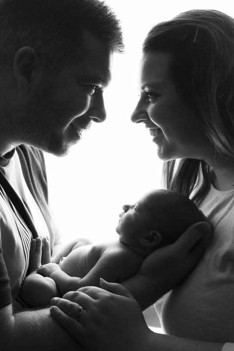 black and white image of Mum and Dad holding newborn baby girl and smiling at eachother New Born Parents Pictures, First Time Family Photos, Couples Newborn Photoshoot, Baby Photo Shoot With Parents, Baby Photo With Parents, Family Portrait Newborn, Black And White Newborn Family Pictures, Studio Newborn Parent Poses, Black And White Newborn Photos