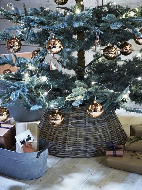 a Christmas tree with copper ornaments and a basket that hides the tree base Rattan Christmas Tree, Christmas Tree Base Cover, Christmas Tree Ring, Navidad Natural, Country Christmas Trees, Christmas Tree Base, Fir Christmas Tree, Tree Base, Tree Ring