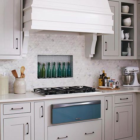 Tuck an alcove between studs and behind the range, then line it with tile to create a kitchen backsplash that doubles as storage. In this kitchen, dressed in soothing gray and blue, hexagonal marble tile and blue linear glass tile converge behind the cooktop for a one-of-a-kind backsplash idea./ Backsplash Options, Honeycomb Backsplash, Backsplash Inspiration, Hex Tiles, Kitchen Tile Backsplash, Niche Market, Unique Kitchen Backsplash, Diy Kitchen Backsplash, White Kitchen Backsplash