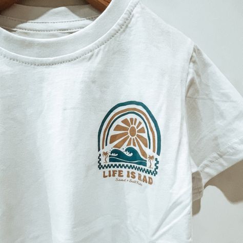 Bring a wave of positivity to your little one's closet with our 'Life is Rad' Kids Tee. This t-shirt, offering a relaxed and true-to-size fit, is perfect for kids on the move. Made from 100% organic cotton, it guarantees comfort and eco-friendliness, aligning with your sustainable lifestyle. With its unique design originating from Phillip Island, Australia, and its careful handcrafting in Bali, this tee is a blend of global quality and local charm. It's not just a tee, it's a statement of cool c T Shirt Boy, Surf Shirt Design, Kids Tees Design, Kids Tshirt Designs, Unique Shirts Design, Minimal Shirt Design, Surf Brands, Surf Tee, Retro Surf