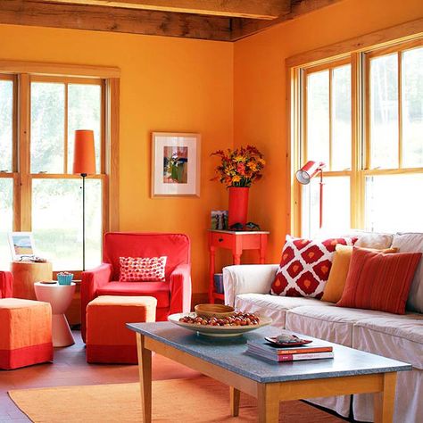 Make an impact with colorful furnishings that don't require permanent commitment. In this lively living room, slipcovers bring saturated color to basic chair and ottoman shapes. A bargain armchair found at an estate sale got a new personality with splashy solid red. A new cube ottoman matches with orange slipcovers banded in red. For a bit of visual relief, the large sofa is slipcovered in plain white. The side table, a tag sale find, gets new life with a coat of bold red paint. Teal And Orange Living Room Decor, Orange Furniture Living Room, Warm Bedroom Colors, Warm Paint Colors, Orange Rooms, Warm Bedroom, Living Room Warm, Living Room Orange, Living Room Color Schemes