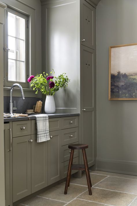 Green mudroom cabinetry with limestone flooring, polished nickel hardware, and dark countertops. Sw Cornwall Slate Cabinets, Sage Kitchen Cabinets Black Hardware, Green Kitchen Cabinets With Brushed Nickel Hardware, Green Cabinets Silver Hardware, Bathroom Green Countertop, Comfort Gray Kitchen Cabinets, Dark Green Mudroom, Muted Green Kitchen, Grey Green Kitchen Cabinets