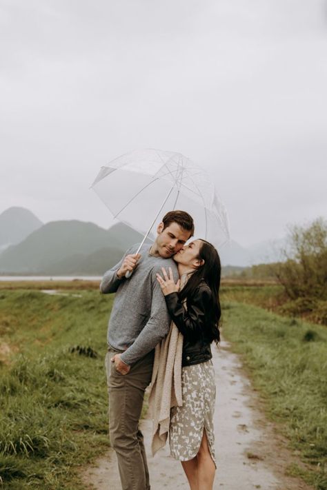 Couple getting cozy in the rain with a clear umbrella while she is kissing him on the cheek. Vancouver Photoshoot, Umbrella Photoshoot, Rainy Photoshoot, Rainy Engagement Photos, Rainy Wedding Photos, Rainy Photos, Rainy Day Photos, Rainy Day Photography, Shooting Couple