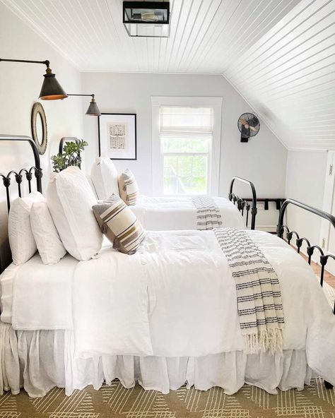 This white beadboard low sloped ceiling bedroom features black metal spindle beds outfitted in white, gray and tan bedding. The beds are lit by black bedroom wall sconces for reading. Gray And Tan Bedding, Sloped Bedroom Ceiling, Sloped Bedroom, Low Sloped Ceiling, Sloped Ceiling Bedroom Ideas, Bedroom Sloped Ceiling, Sloped Ceiling Bedroom, Tan Bedding, Low Ceiling Bedroom