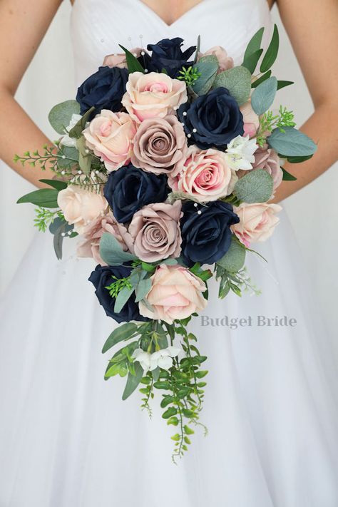 This lovely assortment of navy blue, mauve and pink champagne roses is bound to turn heads on your wedding day. This lovely cascading brides’ bouquet from the is an absolutely breathtaking arrangement for any bride to be, in any season. Sage greenery and accent pearls complete the look and add a delicate realism to this beautiful bouquet. This bouquet is 10” wide, 18” long, and is crafted by our in-house florists without using a foam base to anchor the flowers to the bouquet. Instead, we wire ou Navy And Dusty Pink Wedding, Wedding Navy And Pink, Dark Blue And Pink Wedding, Dusty Blue And Blush Bouquet, Rose Gold And Navy Blue Wedding Theme Wedding Table Decor, Pink And Navy Wedding Flowers, Sage Green Navy Blue Blush Pink Wedding Flowers, Rose Gold And Blue Wedding, Navy Blue And Pink Flowers