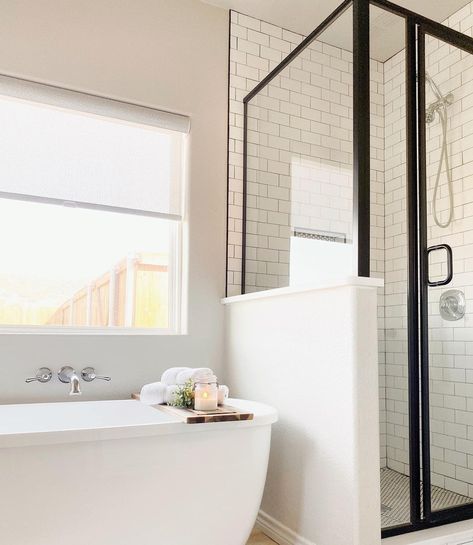 White oval soaking tub and polished nickel wall mounted faucet are positioned under a white picture window with light gray roller shade. A glass black frame half wall shower next to the bathtub features white subway tile walls. Tub Next To Shower Ideas, Shower Next To Tub, White Subway Tile Shower, Mosaic Shower Tile, Half Wall Shower, Tile Shower Niche, White Tile Shower, Ruffle Shower Curtains, Functional Bathroom