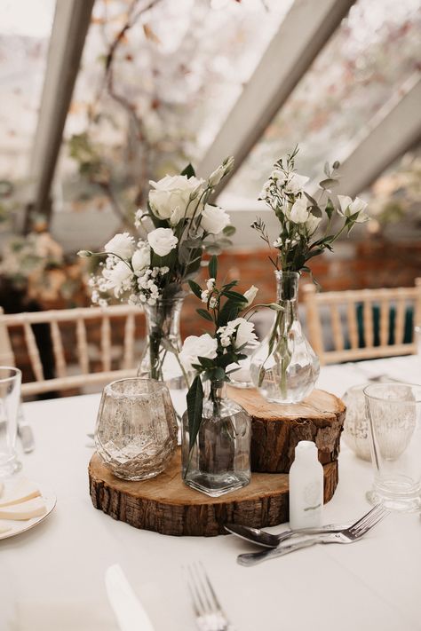 Rustic Wedding Table Centrepieces with White Flowers and Tree Slice Stands Rustic Table Setting For Wedding, Centrepieces Round Table Wedding, Rustic White Wedding Decor, Wedding Small Table Decor, Small Rustic Wedding Decor, Backyard Wedding Table Centerpieces, Tree Slice Centerpiece Wedding, White And Wood Wedding Decor, Wedding Set Up Table