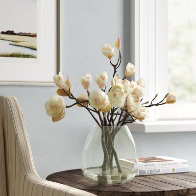 Blossoms that never fade. This faux floral arrangement brings all the freshness and beauty of real flowers to your space without any of the upkeep. Designed to mimic the look of real magnolia blossoms with delicate clusters of white and pink-tinged petals connected to brown, organic-looking branches, they rest in a clear, bell-shaped glass vase that will complement any style of décor. Best of all, the branches are bendable, letting you shape them to suit your style. Flower Color: Pink/Cream | Fr Magnolia Floral Arrangements, Centerpiece Flower, Dining Room Centerpiece, Flower Colour, Coffee Table Centerpieces, Design Showroom, Faux Floral Arrangement, Magnolia Blossom, Faux Flower Arrangements