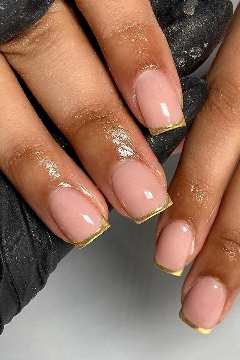 These nails present an elegant take on the classic French manicure with a glossy nude base and striking gold tips. The combination delivers a chic and sophisticated look, perfect for any glamorous occasion.  // Photo Credit: Instagram @gelsbyelisha Gold French Tip Gel Nails, French Nails Gold Tip, Champagne French Tips, Short Gold French Tip Nails, Oval Nails Gold, Nude And Gold Nails Short, Golden French Tip Nails, Gold Tip Nails French, Gold Nails Square