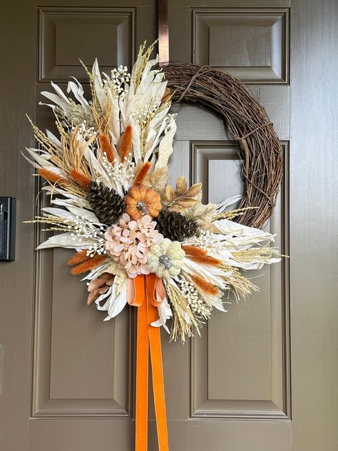 Imagine a fall wreath that perfectly captures the essence of the autumn season. The wreath is lush, with a base of interwoven grapevines, giving it a rustic, natural feel. Nestled among the the corn husk  are various pumpkins , large pinecones and small hydrangea blossoms in neutral shade ,adorned with white berries and burnt orange bunny tail grass picks , all finished with simple orange velvet bow.  The overall effect is both elegant and cozy, evoking the warmth and richness of the fall season. It would make a stunning addition to any front door, welcoming the autumn with style. If hanged outdoors , please insure it is in covered area ,protected from weather elements. Made on 18" grapevine base , finished wreath measures approximately 23-24" in diameter. Please note that grapevine wreath Chic Fall Wreath, Fall Decor For Large Front Porch, Corn Tassel Wreath, Fall Wreaths For Front Door Diy, Boho Thanksgiving, Diy Fall Wreaths, Orange Bunny, Western Wreaths, Corn Husk Wreath