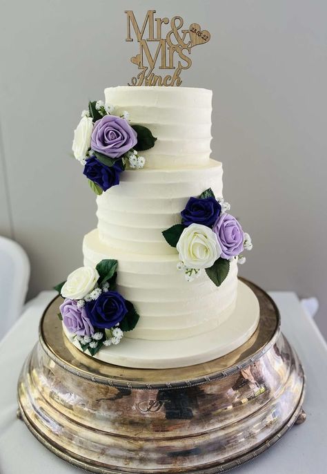 3 tier ridged buttercream wedding cake decorated with clusters of purple, lilac and cream foam roses & artificial leaves & gypsophilia and a personalised topper Navy Blue And Lavender Wedding Reception, Navy Blue And Purple Wedding Cake, Ube Wedding Cake, Wedding Cake Purple And Blue, Simple 3 Tier Wedding Cake, Wisteria Cake, Purple And White Wedding Cake, Lilac Wedding Cake, Wedding Cake Purple Flowers