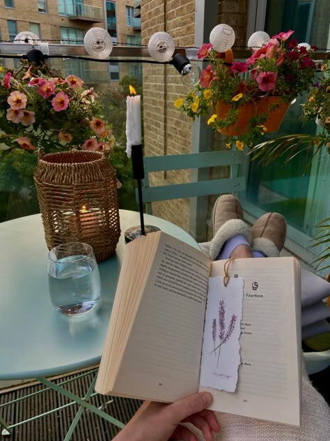 Girl sitting with her feet up reading her book with a handmade watercolor bookmark in on her balcony. The balcony is full of plants and flowers and the sun is setting in the background. Candles are lit and it’s the perfect ending to a day. Reading On Balcony Aesthetic, Slow Living In The City, Reading On Balcony, Books And Plants Aesthetic, Intentional Living Aesthetic, Balcony Candles, Slow Aesthetic, Reading Balcony, Read Books Aesthetic