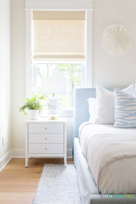 A coastal bedroom painted Sherwin Williams White Duck, one of the best coastal paint colors! This beach house bedroom also features woven roman shades, a light blue upholstered bed, blue and white bed linens, a white nightstand, and white oak hardwood floors. Beach House Ceiling, Best Coastal Paint Colors, Blue Upholstered Bed, Pure White Sherwin Williams, Hola Beaches, Dream Building, Coastal Paint Colors, Coastal Paint, Sherwin Williams White