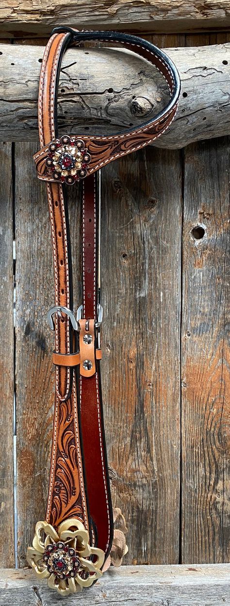 "Roper style, light oil leather one ear headstall. It is full horse size and measures 44\" from bit to bit. Beautifully designed with hand carved floral tooling. We have gussied it up with our superior quality and Eco friendly copper Ruby, Jet, and Champagne SWAROVSKI crystal conchos measuring 1.5\", as well as our hand made gold leather Lotus flower. There are three conchos and two flowers total. We have placed a single concho on the ear and a crystal conho and flower combo at each bit end. Pai Buckaroo Style, Bling Horse Tack, Leather Horse Tack, Cowboy Spurs, Western Headstall, Western Bridles, Saddle Accessories, Gold Lotus, Western Leather