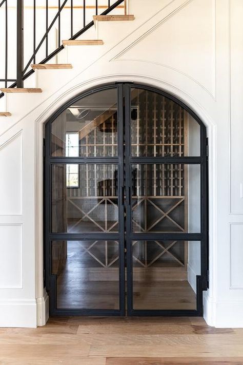 Beautiful arched double doors enter into an under staircase wine cellar surrounded by oak floors and wainscoted walls in a foyer space. Kitchen With Wine Cellar, Kitchen Wine Cellar Ideas, Under Floor Wine Cellar, Cool Staircases, Staircase Wine Cellar, Under Staircase Wine Cellar, Wine Walls, Staircase With Wine Cellar, Wine Room Under Stairs