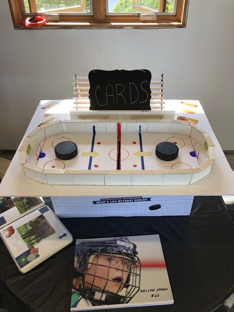 Graduation card box- hockey rink is on thick poster board.  Boards in ice rink are small pieces of plastic used on hockey rinks.  Then use popsicle sticks to make the benches, bleachers, and top of the boards.  Taped a box to the bottom.  Covered the box in hockey paper with double sided tape. Graduation Poster Boards, Senior Poster Board Ideas, Box Hockey, Poster Board Ideas, Graduation Card Box, Hockey Valentines, Senior Poster, Ice Hockey Rink, Graduation Card Boxes