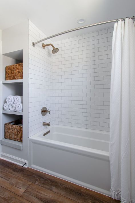 This bathroom features: classic white subway tile, niche with hexagon tile, open shelving, gray cabinetry, quartz counters, plank flooring, a wood mirror Tiled Bathroom Floors And Showers, Bathroom With White Subway Tile, Subway Tile Bathroom Wood Floor, White Bathroom With Tub, Lights Bathroom Ideas, Small Bathroom With Wood Floor, Bathtub Subway Tile Surround, Bathrooms With White Subway Tile, Subway Tile Shower With Tub