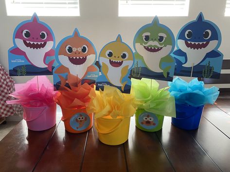 Buckets, tissue paper, dollar tree kabob sticks, dollar tree floral foam, Party City Baby Shark decorations, candy to add weight to the buckets. Baby Shark Pink Party, Baby Shark Birthday Centerpieces, Baby Shark Snack Ideas, Baby Shark Table Centerpiece, Baby Shark 3rd Birthday Party Boy, Baby Shark Diy Decorations, Babyshark Bday Party, Baby Shark Table Decorations, Baby Shark 3rd Birthday Party Girl